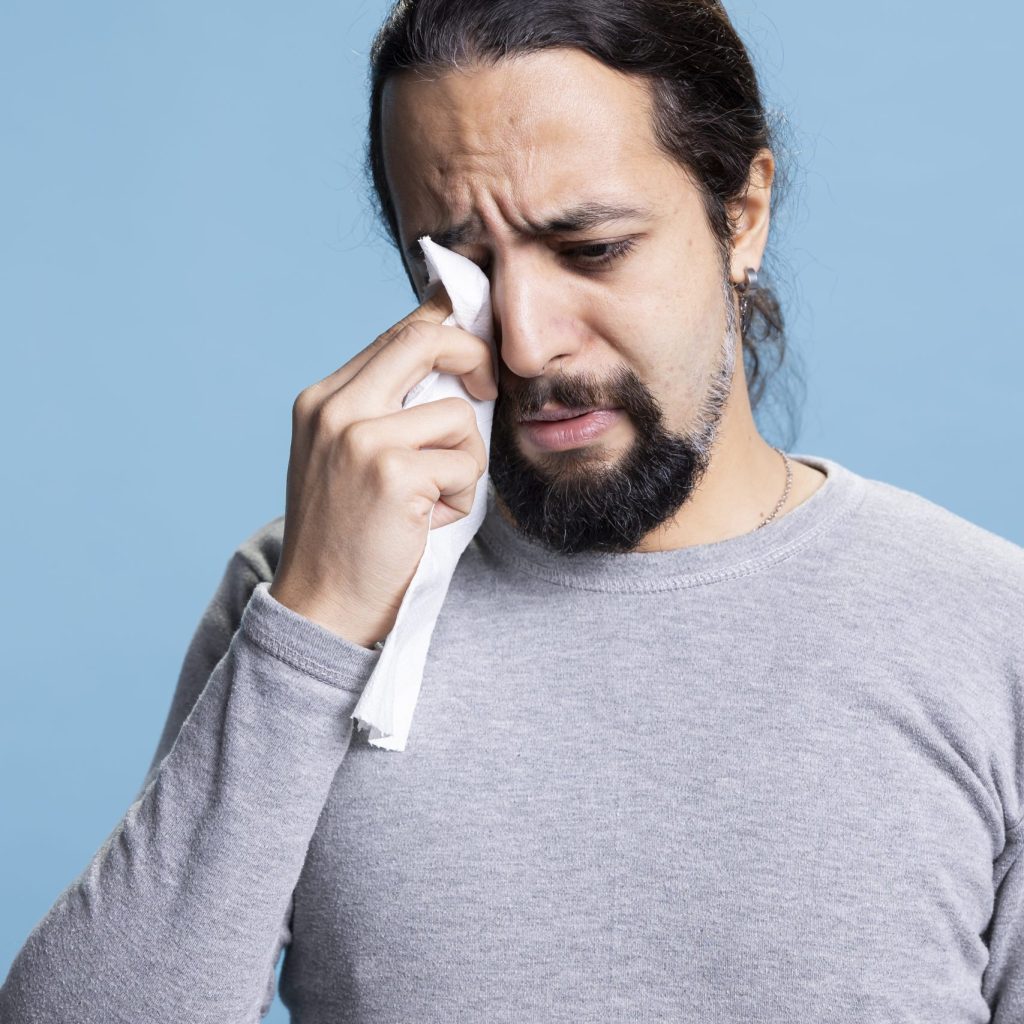 Male model dealing with a heartbreak and crying in studio, wiping his tears with a handkerchief and whining. Young sad man feeling unhappy and distraught, desolation and low self esteem.